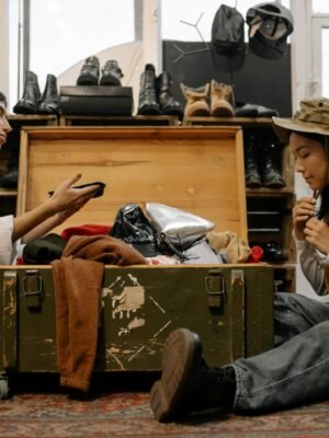 Two women exploring vintage fashion in a cozy thrift store, surrounded by clothes and shoes.